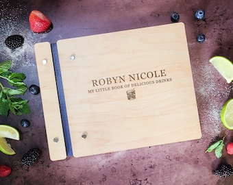 Pode incluir: Um livro de receitas de madeira com uma lombada azul. A capa é gravada com o texto "ROBYN NICOLE MY LITTLE BOOK OF DELICIOUS DRINKS" e um pequeno ícone de copo de coquetel.