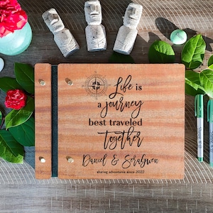 Puede incluir: Un libro de visitas de madera con un dise&ntilde;o de br&uacute;jula y el texto "Life is a journey best traveled together Daniel & Soralgwen sharing adventures since 2022".