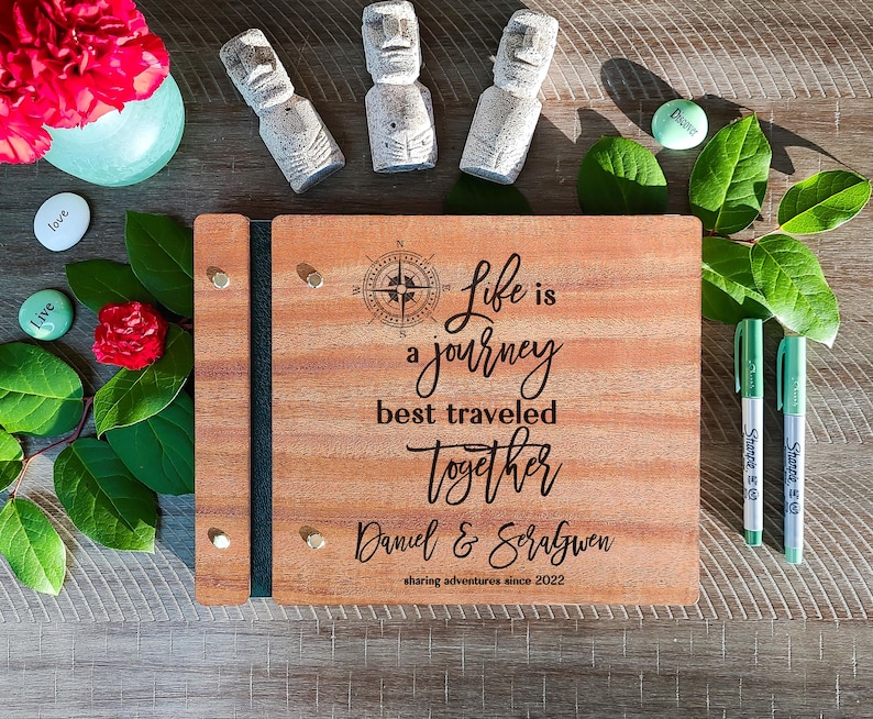 Puede incluir: Un libro de visitas de madera con un dise&ntilde;o de br&uacute;jula y el texto "Life is a journey best traveled together Daniel & Soralgwen sharing adventures since 2022".
