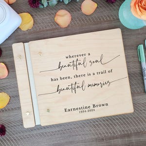 May include: A wooden photo album with a white spine and a quote that reads "wherever a beautiful soul has been, there is a trail of beautiful memories." The album also includes the name "Earnestine Brown" and the dates "1934-2024".