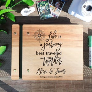Puede incluir: Un libro de visitas de madera con un dise&ntilde;o de br&uacute;jula y el texto "Life is a journey best traveled together Alisa & Javier sharing adventures since 2024".