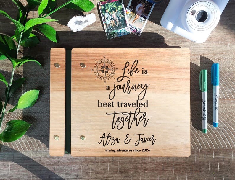 Puede incluir: Un libro de visitas de madera con un dise&ntilde;o de br&uacute;jula y el texto "Life is a journey best traveled together Alisa & Javier sharing adventures since 2024".