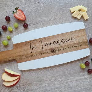 May include: A white and wood serving board with a compass and the text "The Franciszens 33&deg; 52' 1.38" N 84&deg; 27' 52.344" W"