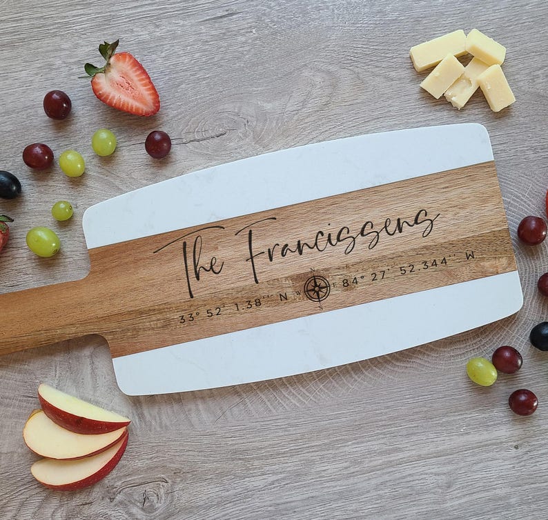 May include: A white and wood serving board with a compass and the text "The Franciszens 33&deg; 52' 1.38" N 84&deg; 27' 52.344" W"