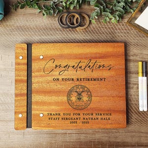 May include: A wooden guest book with a black spine and a laser engraved message that reads "Congratulations on your retirement." The book also features the Department of the Air Force seal and the text "Thank you for your service Staff Sergeant Nathan Hale 2005-2025."