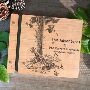 Peut inclure: Un album photo en bois avec une illustration grav&eacute;e d'un enfant, d'un chien et d'un chat sous un arbre. L'album porte l'inscription "The Adventures of Dad, Everett & Kennedy, Happy Father's Day 2025."