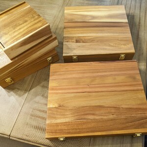 May include: Four wooden boxes with brass hinges. The boxes are stacked on top of each other. The boxes are made of light brown wood with a natural grain pattern.