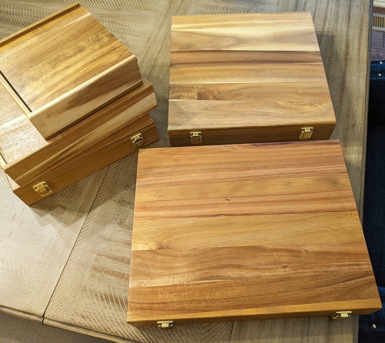 May include: Four wooden boxes with brass hinges. The boxes are stacked on top of each other. The boxes are made of light brown wood with a natural grain pattern.