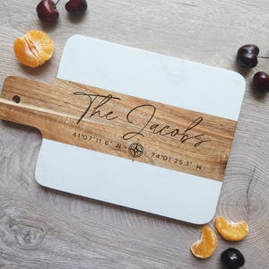May include: A white and brown wooden cutting board with the text "The Jacobs" and coordinates "41&deg;07'11.6" N 74&deg;01'25.1" W" engraved on it.