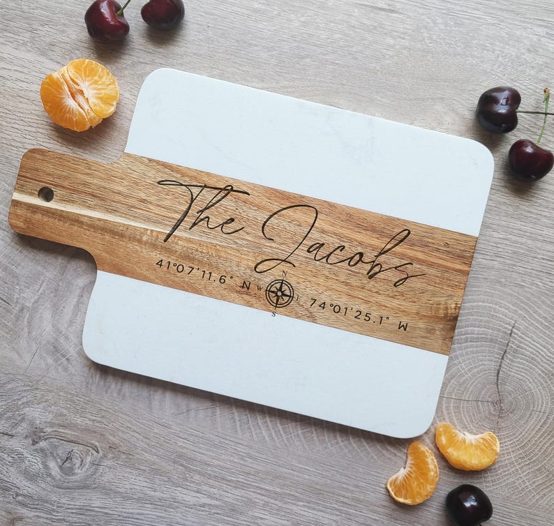 May include: A white and brown wooden cutting board with the text "The Jacobs" and coordinates "41&deg;07'11.6" N 74&deg;01'25.1" W" engraved on it.