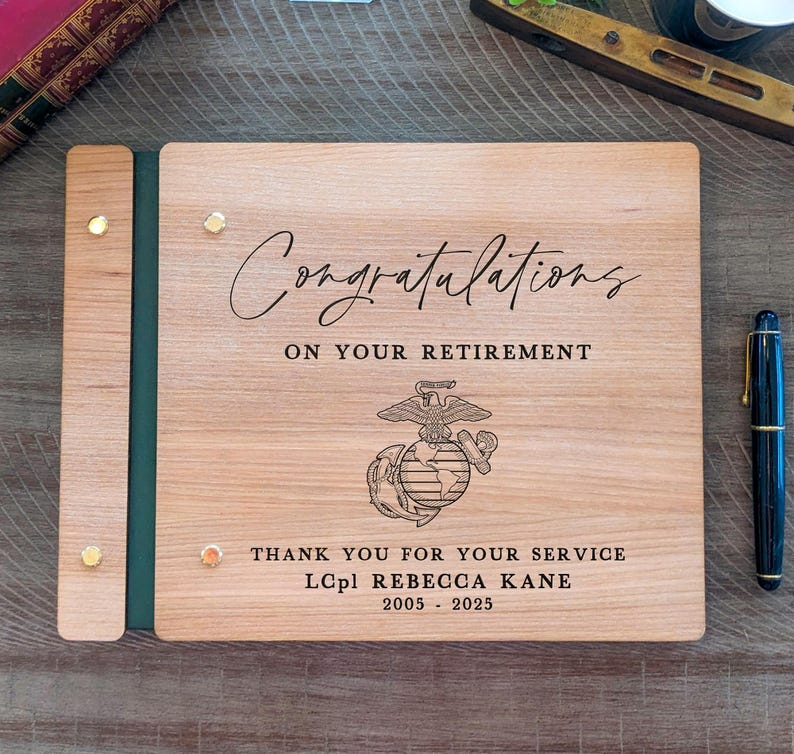 May include: A wooden photo album with a green spine and gold accents. The cover has an engraved message that reads "Congratulations on your retirement." It also features the Marine Corps emblem and the text "Thank you for your service LCpl Rebecca Kane 2005 - 2025."