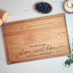 May include: A personalized wooden cutting board with the text "The Santiagos home sweet home 36° 20' 49.56" N 119° 42' 22.068" W" engraved on it.