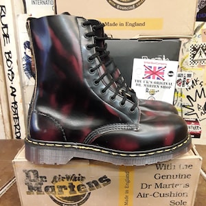 May include: Black leather Dr. Martens boots with yellow stitching and a red and blue marbled pattern. The boots are on a box that says "Dr. Martens" and "With the Genuine Dr. Martens Air-Cushion Sole".
