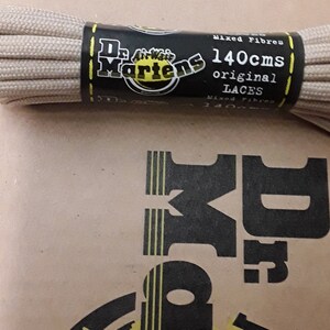 May include: Beige shoelaces in a plastic package with a black label that says "Dr. Martens AirWair 140cms original LACES Mixed Fibre 140cms".