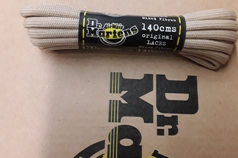 May include: Beige shoelaces in a plastic package with a black label that says "Dr. Martens AirWair 140cms original LACES Mixed Fibre 140cms".