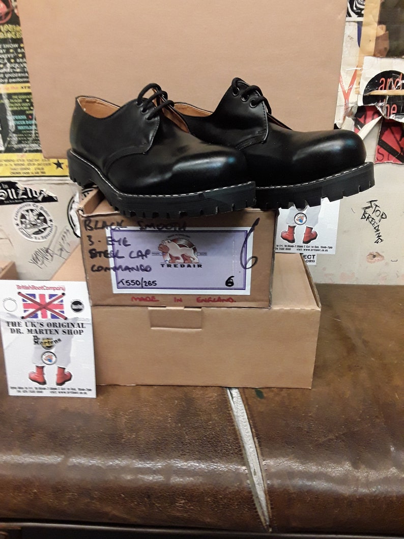 May include: Black leather lace-up shoes with a thick sole. The shoes are on a box with the text "Black Smooth 3-EME Steel Cap Commando K550/265 Made in England 6" on it.