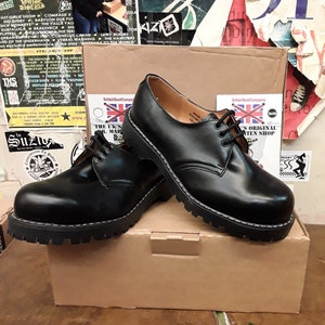May include: A pair of black leather lace-up boots with a thick, black rubber sole. The boots are sitting on a brown cardboard box with the text "British Boot Company" and "The UK's Original Boot Shop" printed on it.
