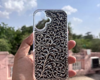 Puede incluir: Funda transparente para teléfono con un diseño floral plateado sobre un fondo oscuro. La funda tiene un borde transparente y se muestra contra un cielo azul.