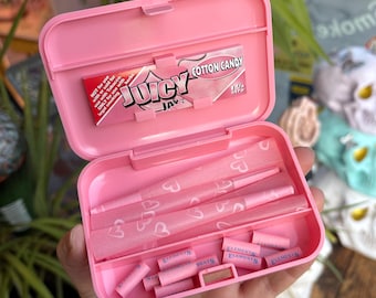 May include: A pink plastic box with the words "Juicy Jay Cotton Candy" on a red and pink package. The box contains pink pre-rolled cones and pink filter tips. The cones have a heart pattern.