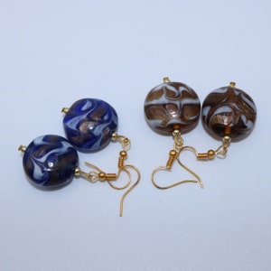 Peut inclure: Une paire de boucles d'oreilles avec des crochets dorés et des perles de verre rondes. Les perles sont bleues et blanches avec un motif en spirale, et brunes et blanches avec un motif en spirale.