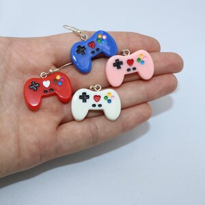 Puede incluir: Cuatro pares de pendientes de mando de juego de colores. Los pendientes están hechos de arcilla polimérica y presentan una variedad de colores, incluyendo rojo, azul, rosa y blanco. Cada pendiente tiene un pequeño corazón en el centro del mando.