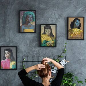 Może przedstawiać: Cztery oprawione portrety kobiet w ubraniach w stylu vintage. Portrety są w czarnych ramach i przedstawiają kobiety o ciemnych włosach i kolorowych ubraniach. Portrety wiszą na szarej ścianie.