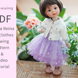 May include: A doll wearing a white jacket and a lavender tulle skirt with silver sparkles. The doll has brown hair and is surrounded by greenery. Text on the image reads "Rosysewing PDF Paola Reina doll clothes sewing pattern & Video tutorial."
