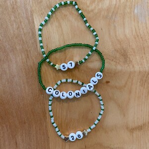 May include: Three green and white beaded bracelets with white letter beads spelling "COLONIALS" and the numbers "51" and "20".