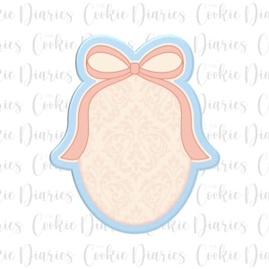 May include: A bell-shaped cookie cutter with a bow at the top. The cutter is outlined in light blue, with a peach-colored bow and ribbons. The interior of the bell has a light peach damask pattern.