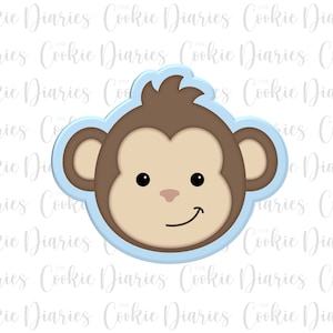 May include: A blue and brown cookie cutter shaped like a monkey's face. The monkey has a brown face, brown hair, and a light brown nose. The monkey is smiling.