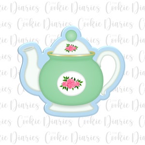 May include: A cookie cutter in the shape of a teapot. The teapot is light green with a gold rim and a white spout and handle. Pink roses decorate the lid and the body. The cutter is outlined in light blue.