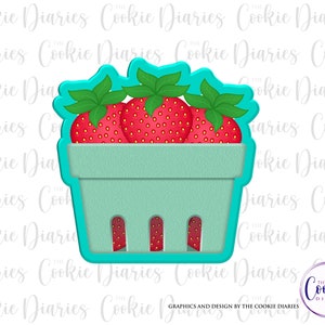 May include: A cookie cutter in the shape of a strawberry container with three strawberries inside. The container is light blue and the strawberries are red with green leaves.