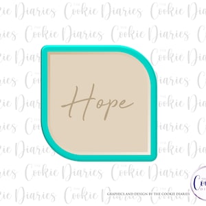 May include: A turquoise blue cookie cutter shaped like a rounded rectangle with the word "Hope" written in brown inside.
