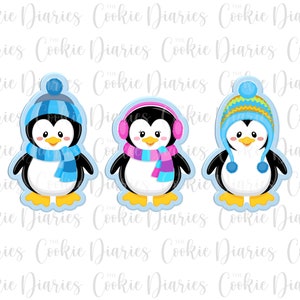 May include: Three penguin cookie cutters, each wearing a different winter hat. The penguin on the left is wearing a blue hat and scarf. The penguin in the middle is wearing a pink hat with earmuffs. The penguin on the right is wearing a yellow and blue striped hat.