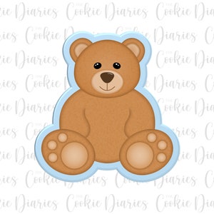 May include: A blue cookie cutter shaped like a brown teddy bear sitting with its paws in front of it.