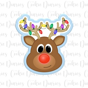 May include: A brown reindeer cookie cutter with a red nose and big eyes. The reindeer has a string of colorful lights on its antlers. The cookie cutter is on a light blue background.