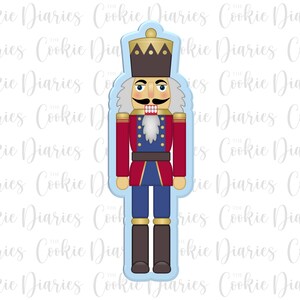 May include: A blue and red nutcracker cookie cutter with a white beard and a gold crown. The cookie cutter is in the shape of a traditional nutcracker.