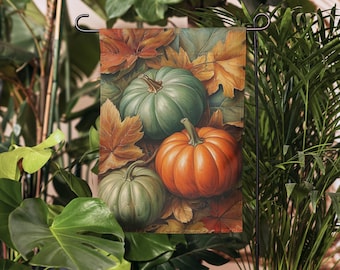 May include: A garden flag featuring a fall harvest scene. The flag displays three pumpkins in shades of green and orange, surrounded by autumn leaves. The flag is mounted on a black metal stand, perfect for outdoor decor.