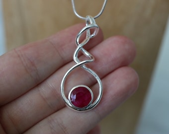 Op de afbeelding: Een zilveren hanger met een gedraaid ontwerp en een rode edelsteen in het midden.
