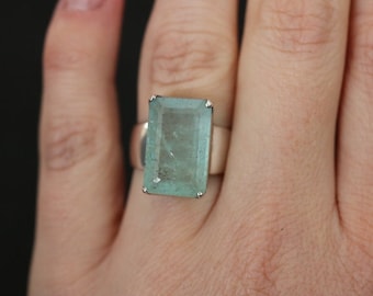 May include: A silver ring with a large, light blue, emerald-cut gemstone.