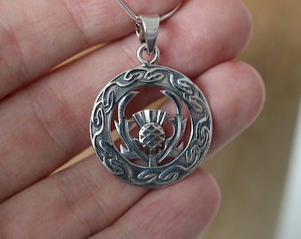 Puede incluir: Colgante de plata con un diseño de nudo celta detallado y un cardo estilizado en el centro.