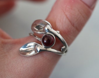 May include: A silver ring with a red gemstone set in a leaf design.