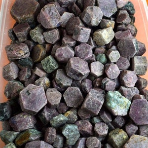 Puede incluir: Una colección de cristales de piedras preciosas en bruto, de color púrpura y verde. Los cristales son de varios tamaños y formas, algunos tienen una forma hexagonal.