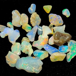 May include: A collection of small, iridescent opal gemstones in various shapes and sizes. The opals are a mix of white, blue, green, and brown.