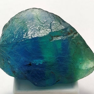 May include: A large, rough-cut blue and green fluorite crystal. The crystal has a translucent appearance and shows banding of blue and green colors.