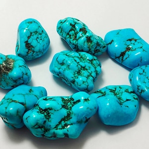 May include: A collection of nine turquoise stones, each with a unique shape and pattern of blue and green veins. The stones are smooth and polished, with a natural, earthy look.