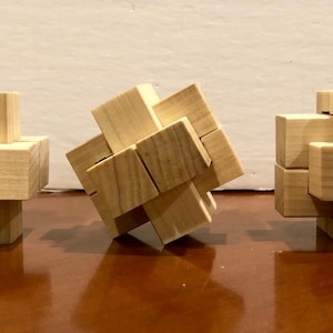 May include: Three wooden burr puzzles of varying configurations. The puzzles are constructed from interlocking wooden blocks, showcasing a natural wood grain. The puzzles are designed to challenge and engage the mind, offering a classic brain teaser experience.