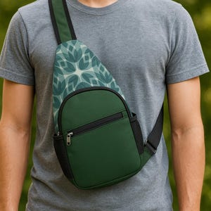May include: Green sling bag with a black zipper and a patterned strap. The bag has a small pocket on the side and a black strap. The pattern on the strap is a light blue floral design.