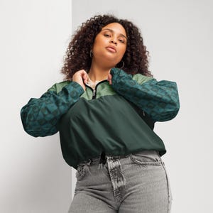 May include: A green and teal windbreaker jacket with a half-zip closure and a drawstring hem. The sleeves feature a geometric pattern, and the jacket is worn with gray jeans.