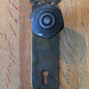 Könnte beinhalten: Antiker Türknauf aus Messing mit einem dekorativen Schlüsselloch und einem runden, schwarzen Knauf. Der Knauf hat ein dekoratives Design am Rand.